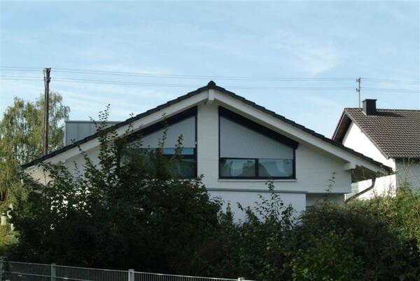 Modernes Einfamilienhaus mit Satteldach, weißen Fassaden und geschlossenen Rollläden.