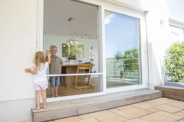 Zwei Kinder spielen an einer großen, modernen Terrassentür mit Blick ins helle Wohnzimmer.
