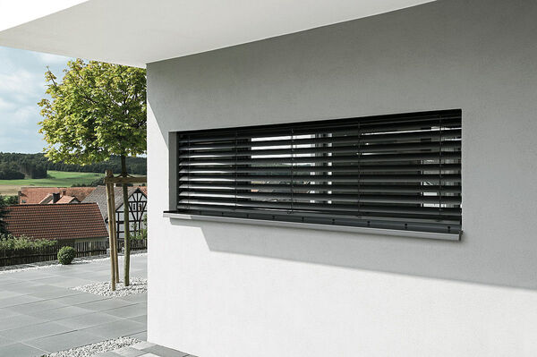 Modernes Haus mit anthrazitfarbenem Raffstore am Fenster und Ausblick auf Garten und Dächer.