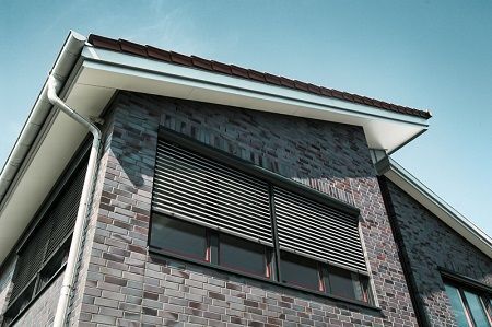 Modernes Haus mit Klinkerfassade und außenliegenden Jalousien am Fenster im Sonnenschein.